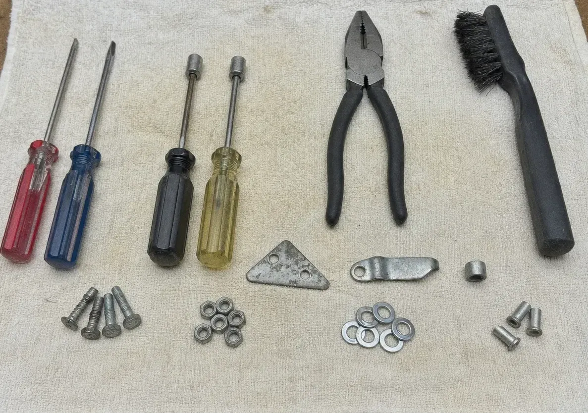 Four screwdrivers, two nut drivers, lineman’s pliers and a wire brush laid out with bolts, nuts and washers in tidy groups